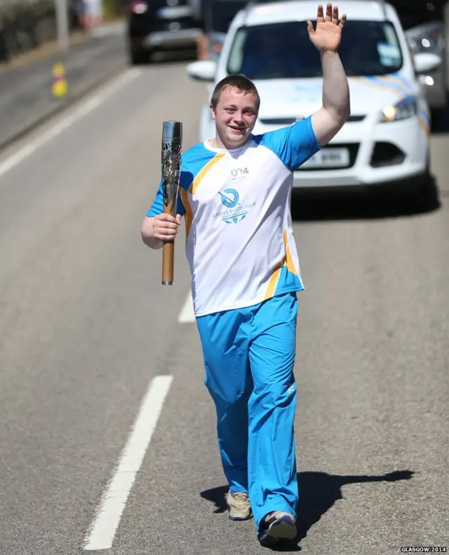 Jamie Gunn waves as he carries Queen's baton