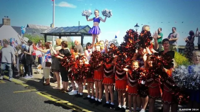 A row of cheerleaders waving pom-poms at the side of the baton route.