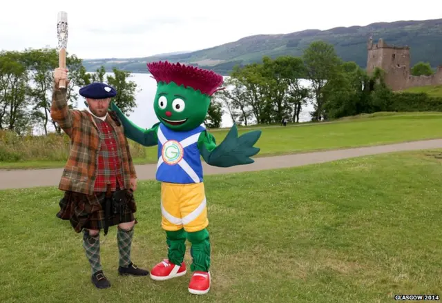 Commonwealth Games mascot Clyde poses with man in full Highland dress with Urquhart Castle in the background