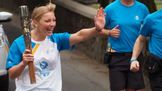 Kareena Marshall waves to fans asshe runs with the baton through Quarrier's Village.