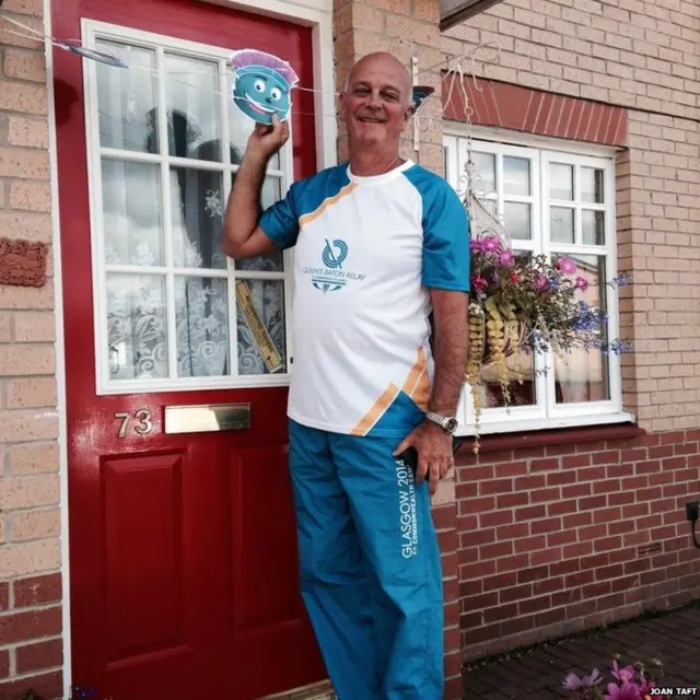 Baton bearer poses on doorstep holding miniature Clyde cut out.