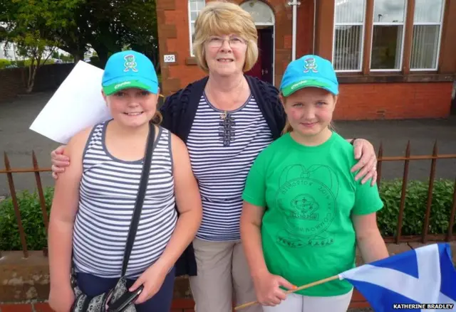 Grandmother with granddaughters, who are wearing Clyde hats and carrying Scottish flags