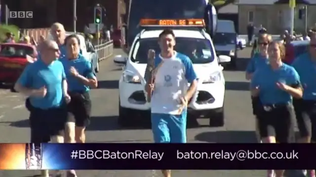 Screengrab of baton relay video feed showing Kenneth Bain running with baton