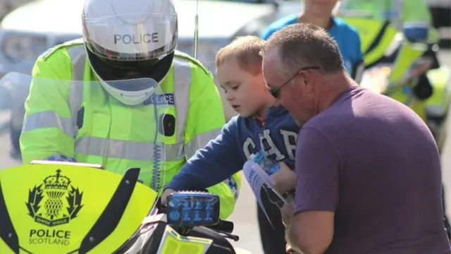 Small boy presses button on police motorcycle as officer looks on