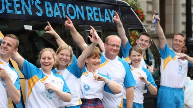 Row of baton bearers doing the Usain Bolt point to the sky, one is pointing in the opposite direction