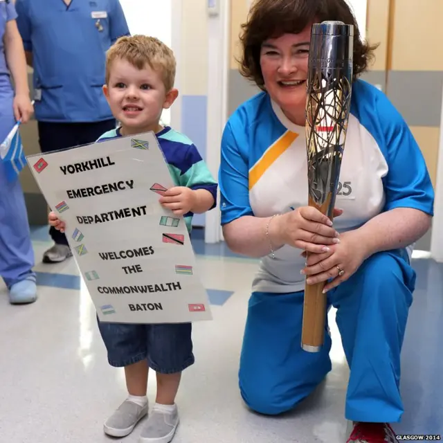 Baton bearer Susan Boyle kneels beside young boy who holds placard saying "Yorkhill emergency department welcomes the Commonweatlh baton"