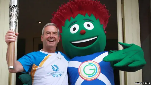 Baton bearer poses with Clyde, the anthropomorphic thistle mascot of Glasgow 2014