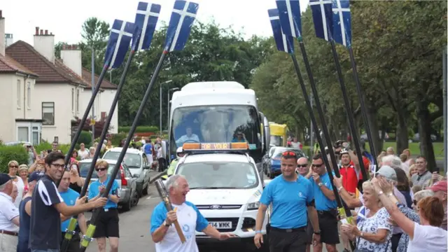 Baton bearer walks under archway of oars