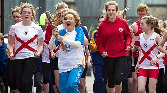 Fictional baton bearer runs with group of young athletes