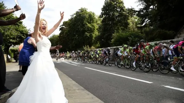 A woman wearing a bride dress waves as the pack rides during the 137.5 km 21st and last stage