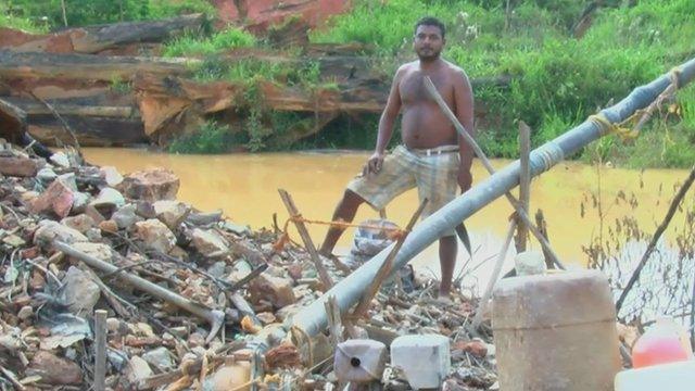 man standing on heap of rocks and rubbish next to stagnant pool