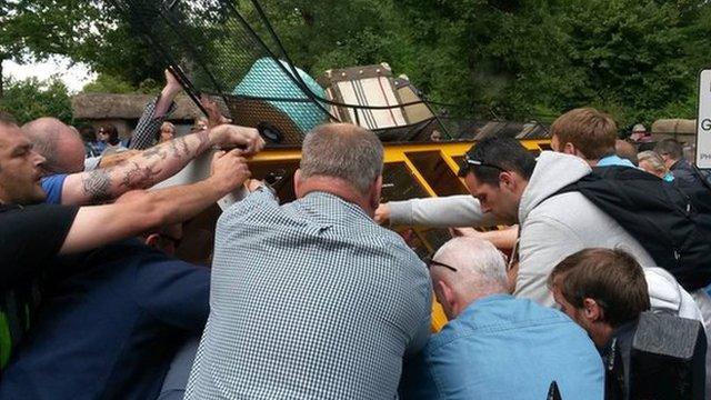 People at the adventure park try to get the tipped train back on its wheels