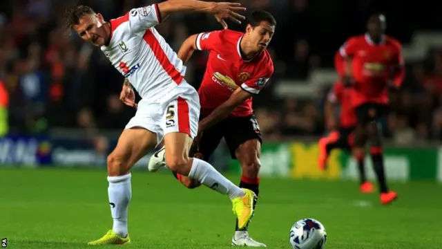 Millton Keynes Dons' Antony Kay tussles with Manchester United's Javier Hernandez