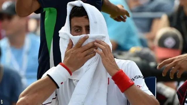 Novak Djokovic of Serbia wipes his face during a break in play