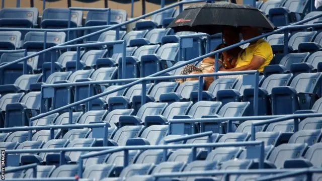 Fans shelter under umbrellas during a rain delay