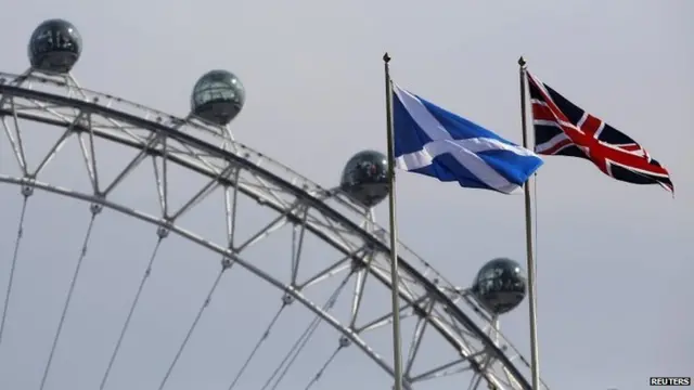 A Scottish Saltire flag and British Union flag fly together with the London Eye behind in London