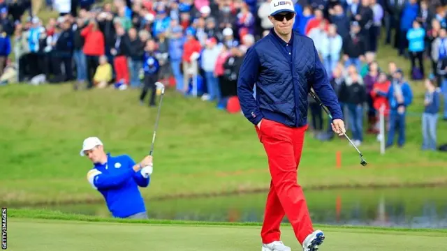 Hunter Mahan of the United States walks to mark his ball with Justin Rose of Europe in the bunker