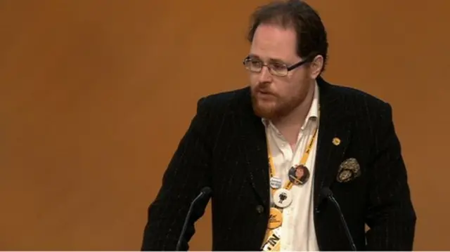 Alasdair McGregor, a Lib Dem councillor, shows off his badge collection, as he addresses activists on climate change and flooding.