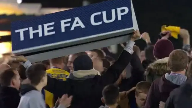 A fan holds a FA Cup advertising hoarding aloft