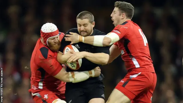 New Zealand hooker Dane Coles is tackled by Wales' Jake Ball (L) and Alex Cuthbert (R)