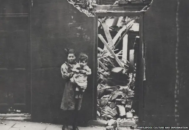 A young girl holding a small child outside a shell damaged house in Sussex Street