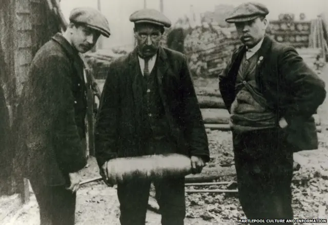 Three men, one is holding an unexploded 5.9 shell, which was found in the railway sidings in Hartlepool