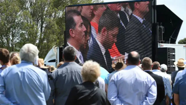 A crowd watches the funeral from the school oval in Macksville