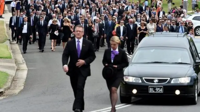 A large procession of mourners walk through the streets of Macksville