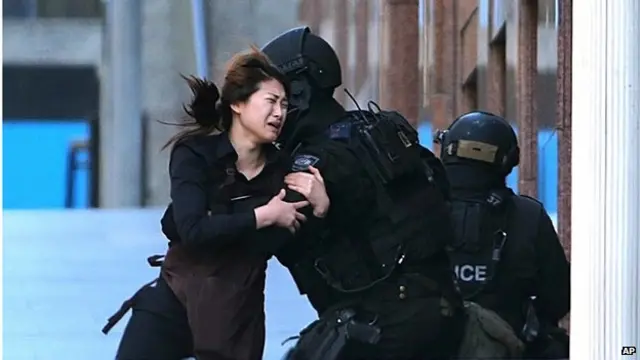 A hostage runs to armed tactical response police officers for safety after she escaped from a cafe under siege at Martin Place in the central business district of Sydney, Australia, Monday, 15 December 2014