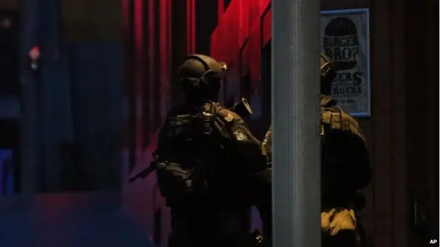 Armed tactical response police personnel stand watch into the evening near a cafe under siege by a gunman at Martin Place in the central business district of Sydney, Australia, on 15 December 2014