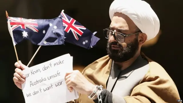 Man Haron Monis bound in chains and holding an Australian flag outside a Sydney court after being charged with seven counts of unlawfully using the postal service to harass families of Australian soldiers (10 November 2009)