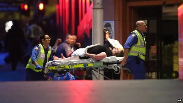 A injured hostage is wheeled to an ambulance after shots were fired during a cafe siege at Martin Place