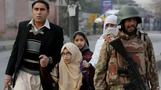 Pakistani parents - accompanied by a soldier - rush their children to safety