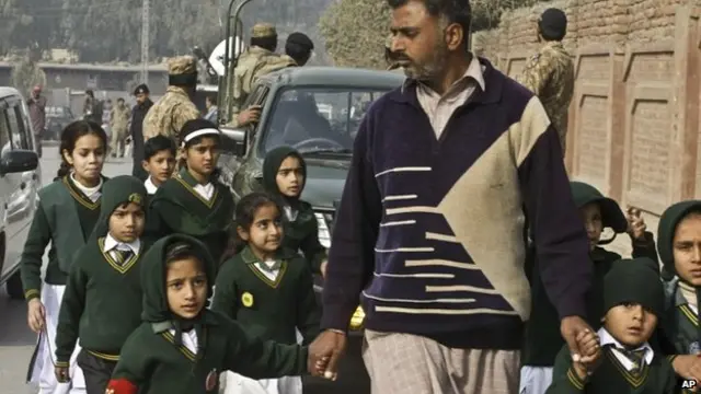 A plainclothes security officer evacuates pupils from a school close to the one attacked by the Taliban militants in Peshawar