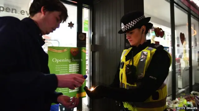 A police officer helps to light candles at the scene of a bin lorry crash in George Square