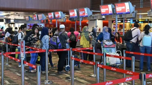 Passengers queue at the AirAsia check-in counter before departure at Singapore Changi airport terminal on 28 December, 2014