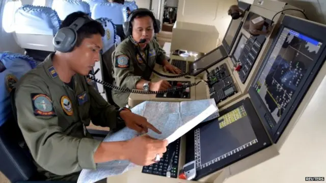 Two members from the Indonesian Navy's Tactical Commanding Operator (TACCO) help with the search for AirAsia flight QZ 8501 on board a CN235 aircraft over Karimun Java in the Java Sea on 28 December 2014