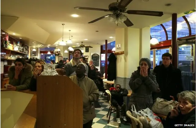 People watch on TV in a cafe as police mobilize at the hostage situation at Port de Vincennes on January 9, 2015