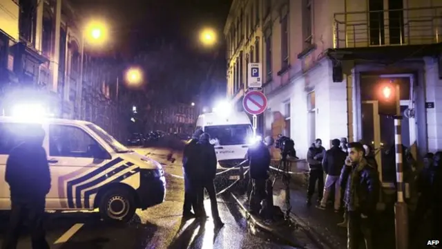 Journalists and local residents stand near police vehicles as police set a large security perimeter in the city center of Verviers on January 15, 2015