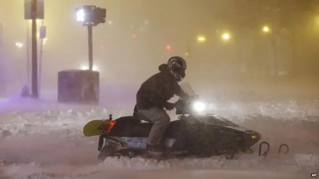 A man uses a snowmobile to travel along a street before dawn during a winter snowstorm 27 January 2015