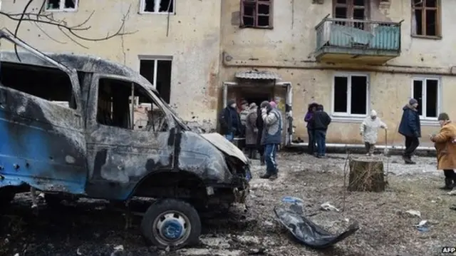 People clean a street near a destroyed car after shelling in the Leninsky district of the eastern Ukrainian city of Donetsk, 8 February 2015