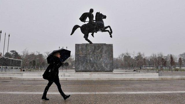 A woman walks past the statue of Alexander the Great under the shelter of her umbrella as snow falls in Thessaloniki on February 9, 2015