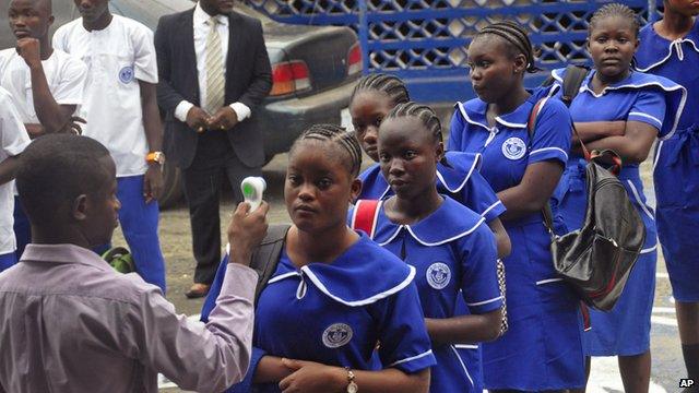 A Liberian school teacher, left, takes the temperature of students as they arrive for morning lessons at school in Monrovia, Liberia, on 16 February, 2015