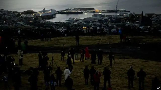 People watch as darkness falls during the totality of a solar eclipse on a hill beside a hotel on the edge of the city overlooking Torshavn, the capital city of the Faeroe Islands