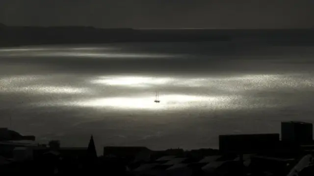 A spot of sunlight breaks through the clouds and shines on a vessel on the sea during the partial phase of a solar eclipse before totality.