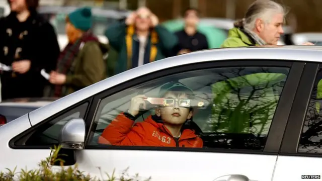 A boy holds protective glasses as he watches a partial solar eclipse from the grounds of Belfast Zoo.