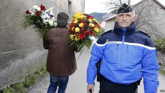 A man passes by a police officer to deliver flowers to the gymnasium set up as a makeshift chapel to welcome families of the victims in Seyne-les-Alpes, south-eastern France