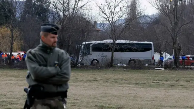 A soldier stands guard in a field as a coach transporting relatives of the victims arrives in Seyne-les-Alpes