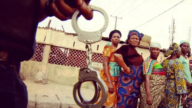 Women looking at a security official holding handcuffs in Lagos