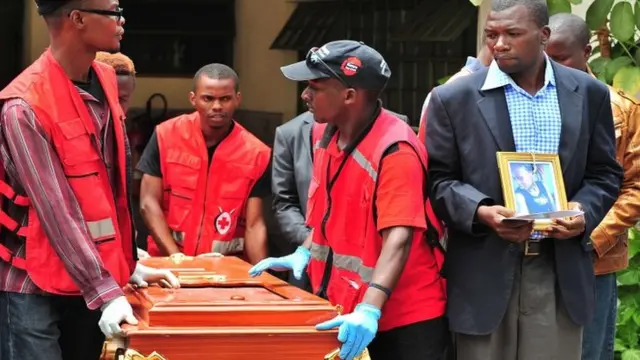 A relative holds a potrait of his relative as he watches her coffin being rolled out by Kenya Red Cross personnel at Chiromo funeral parlour in nairobi,